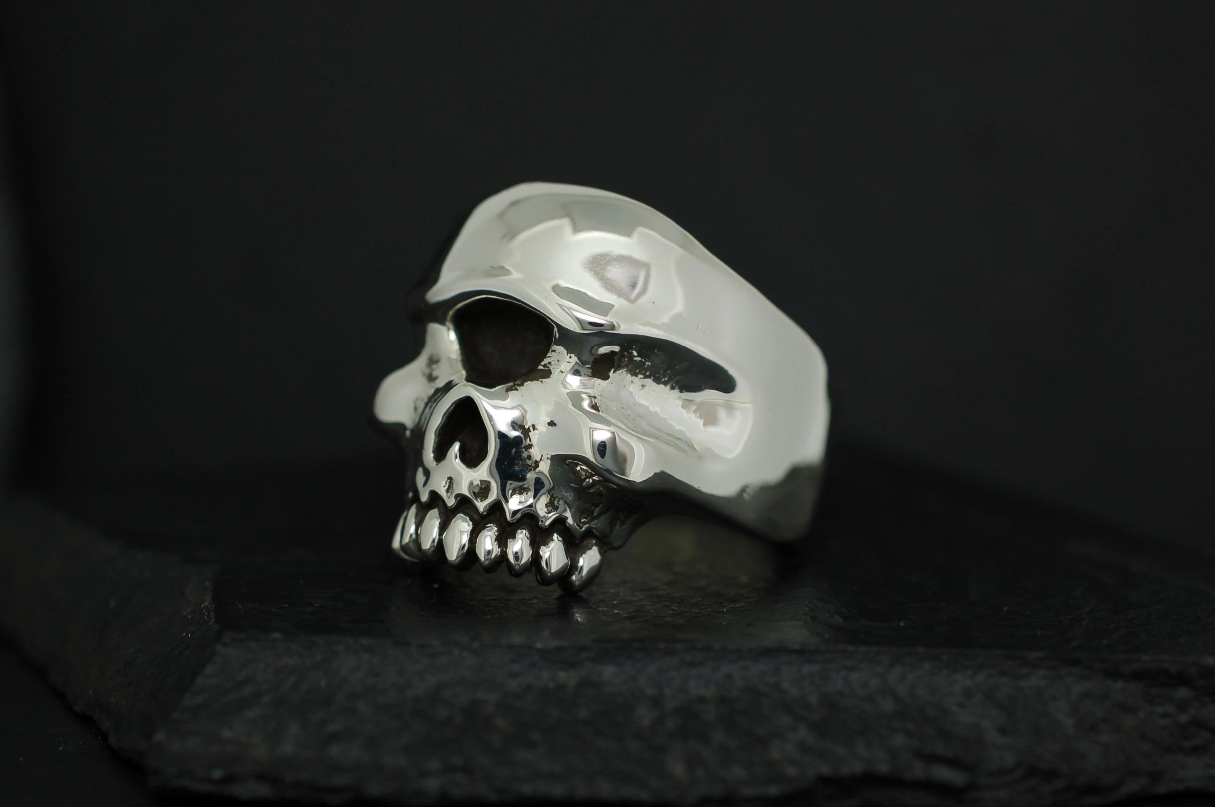 A silver skull-shaped ring with detailed teeth on a black background.