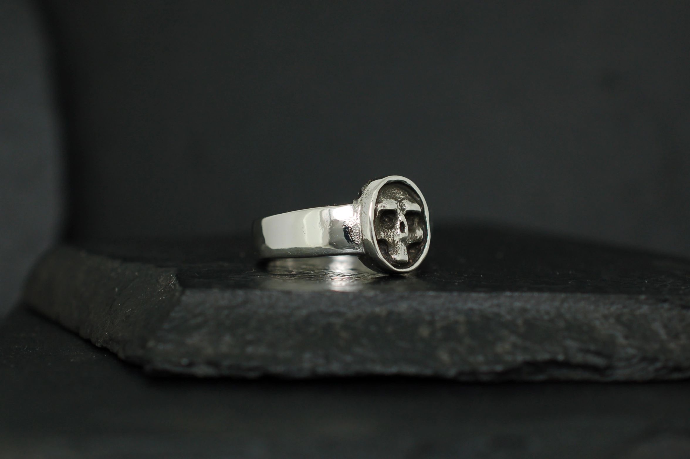 Silver ring with a unique circular emblem on a dark surface.