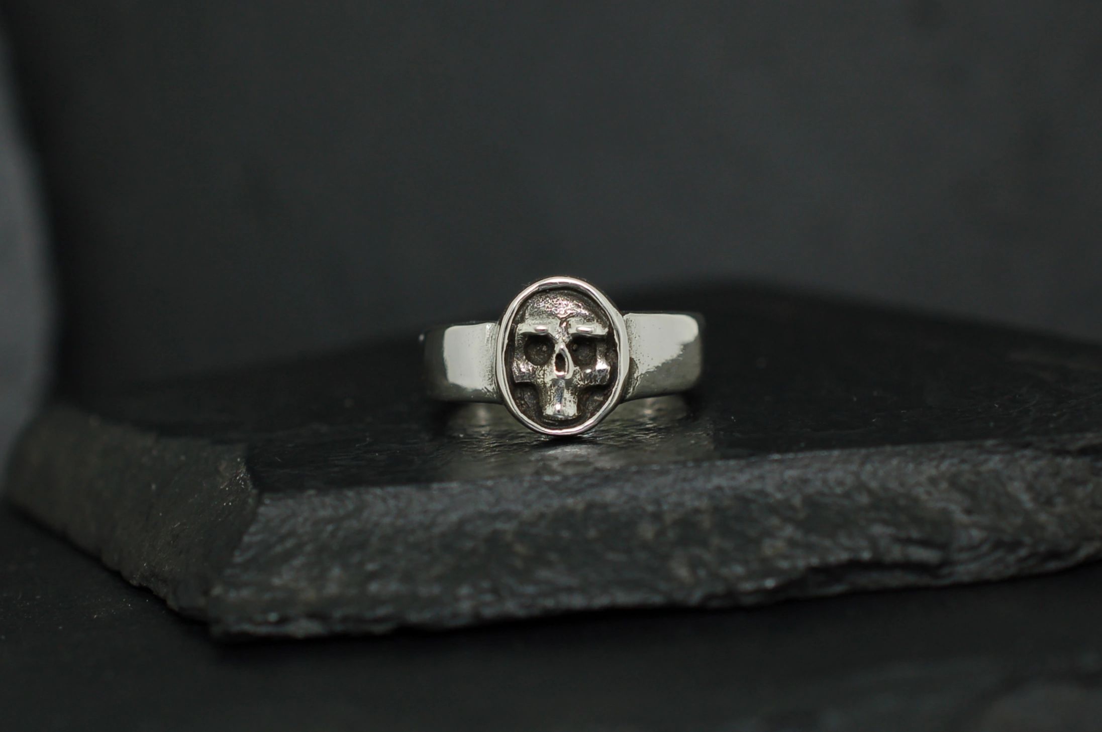 Silver ring featuring a detailed skull design on a dark background.
