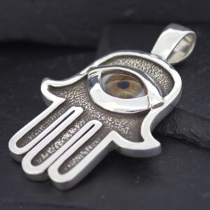 Silver Hamsa hand pendant with an eye design on a black background.