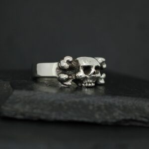 Silver ring with a skull design on a dark surface.