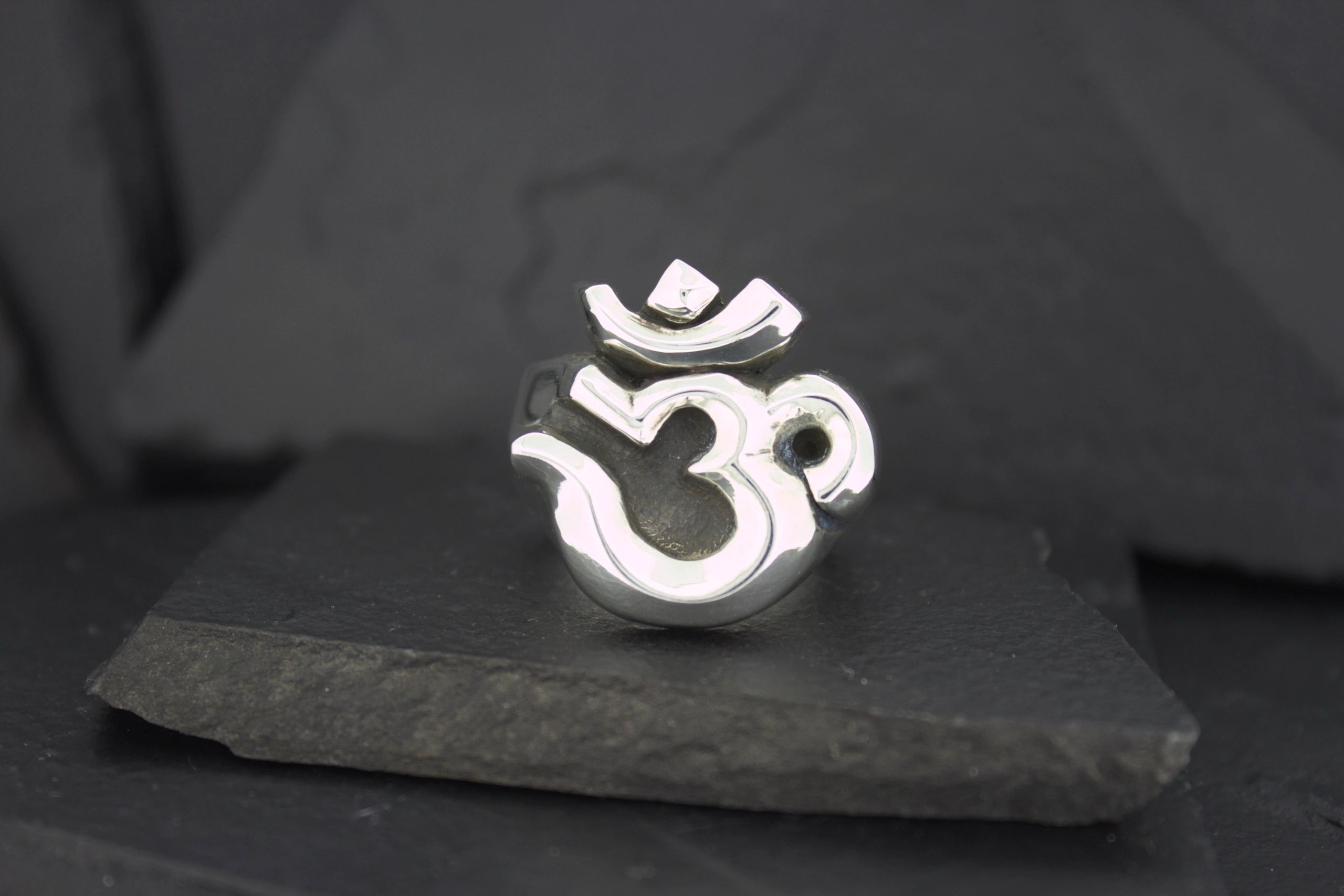 Silver Om symbol pendant on a black surface.