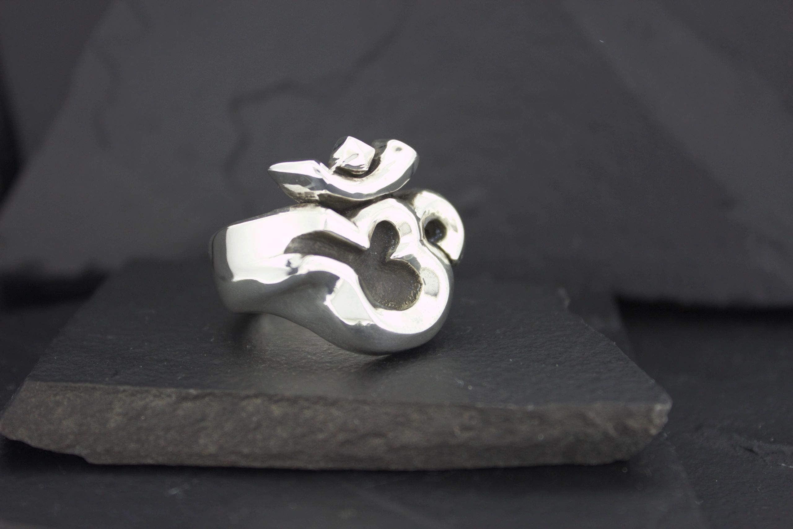 A silver ring featuring the Om symbol on a dark background.