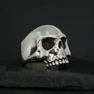 A polished silver skull ring on a dark surface.