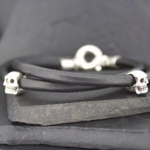 Black leather bracelet with silver skull accents on a dark slate background.