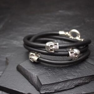 Black leather bracelets with silver skull beads on a dark slate surface.