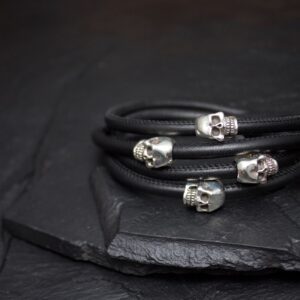 Black leather bracelets with silver skull charms on a dark surface.