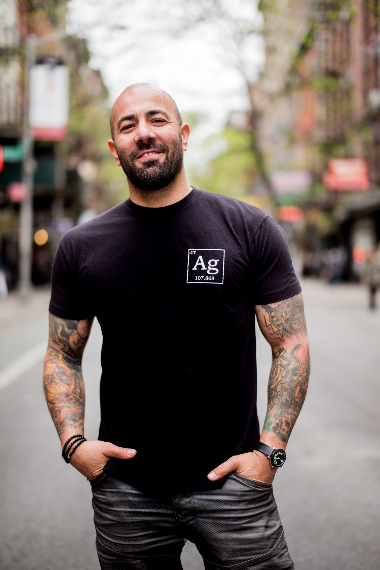Man with tattoos wearing a black shirt with 'Ag' logo outdoors.