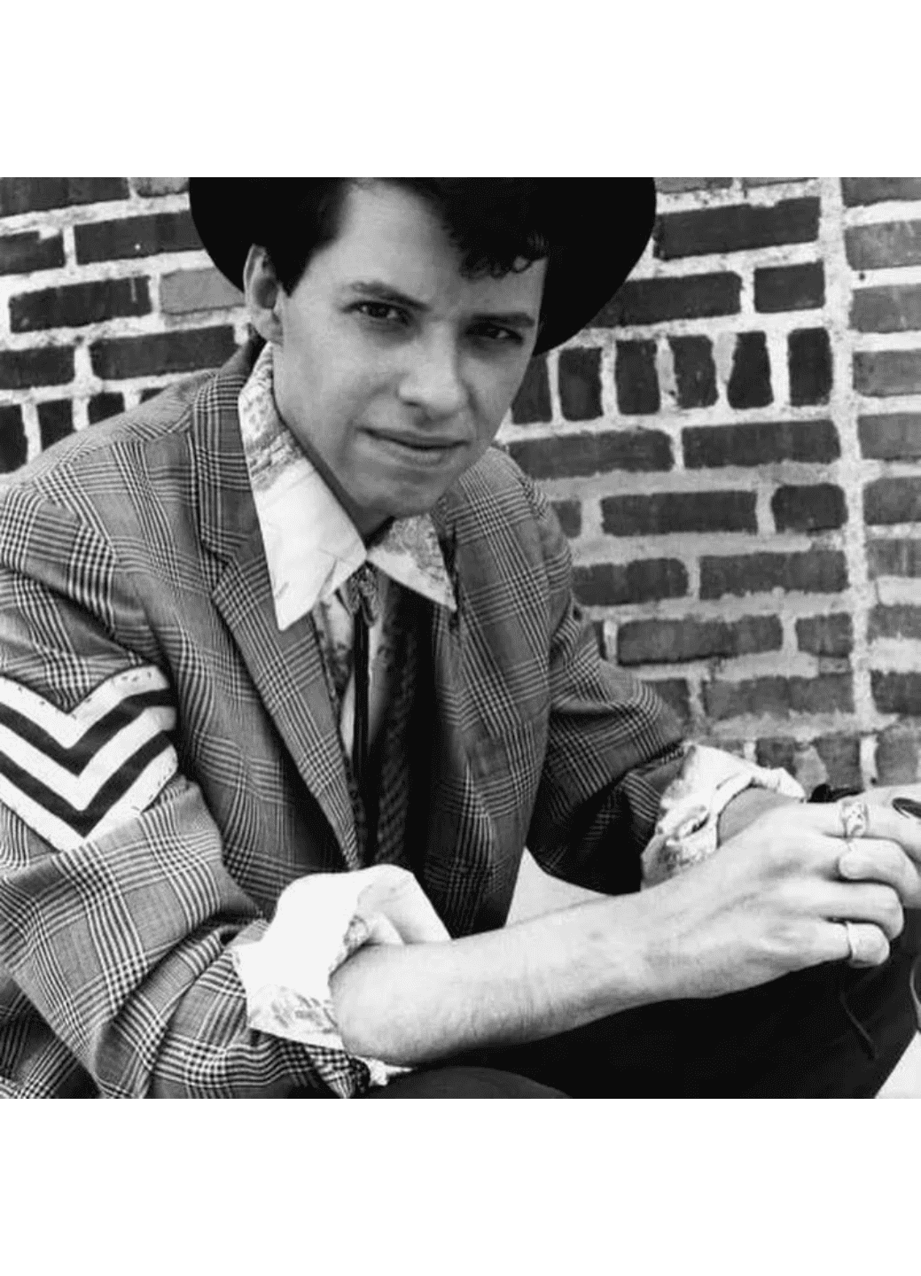 Black and white photo of a young man in a vintage uniform sitting outdoors.