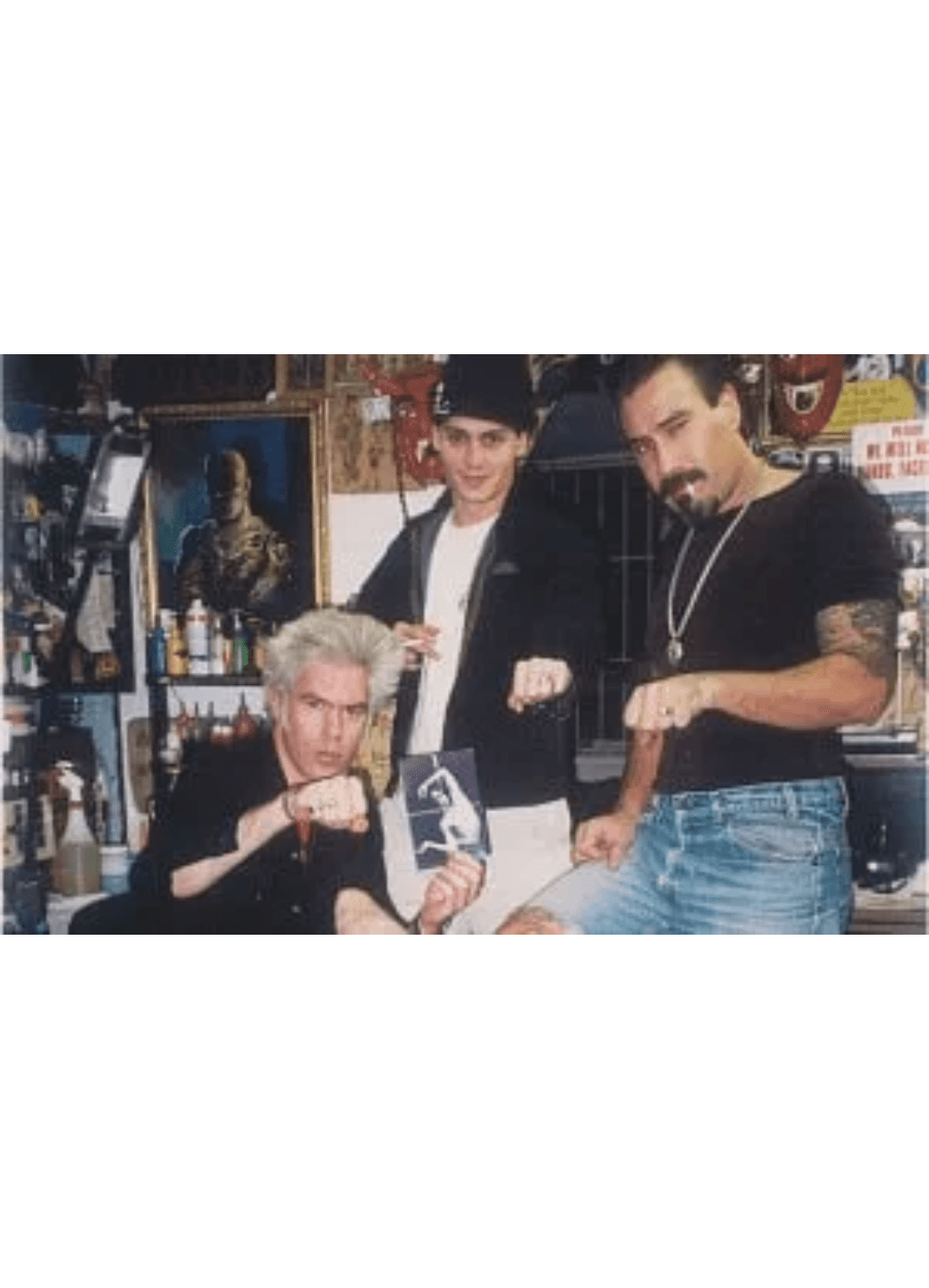 Three people posing in a casual, retro-style room with various posters.