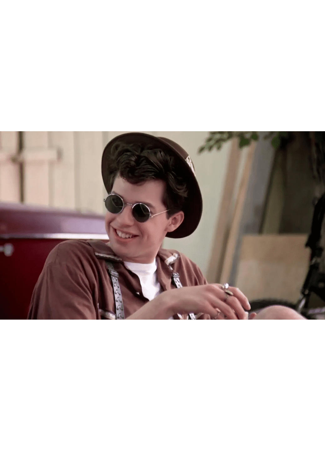 Young man wearing sunglasses and a hat, smiling at a laptop.