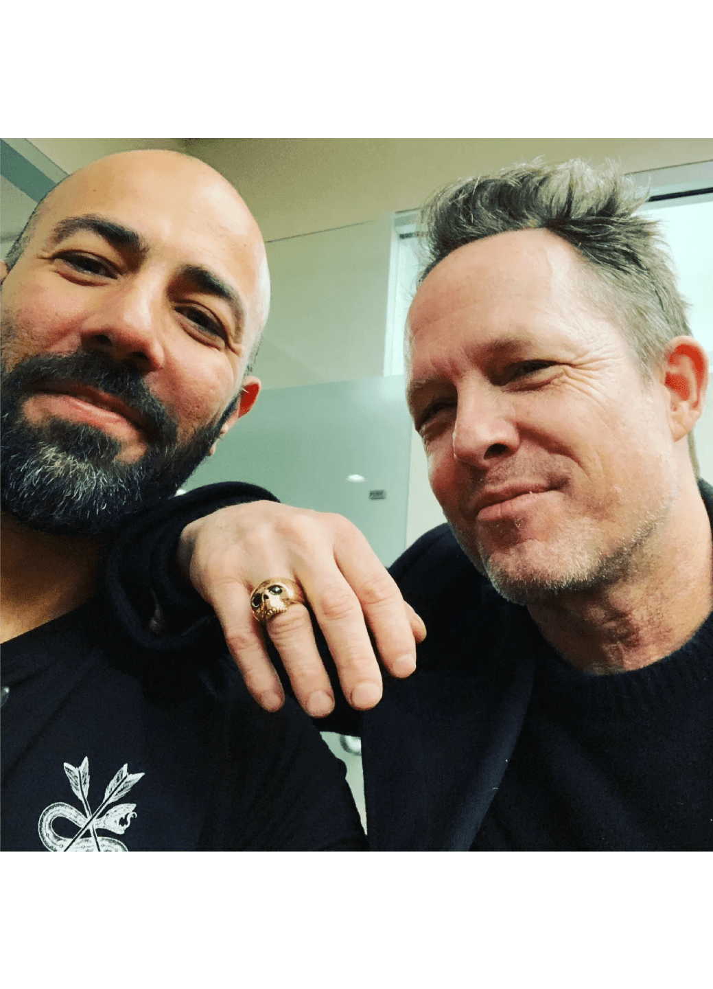 Two men smiling closely for a selfie indoors.