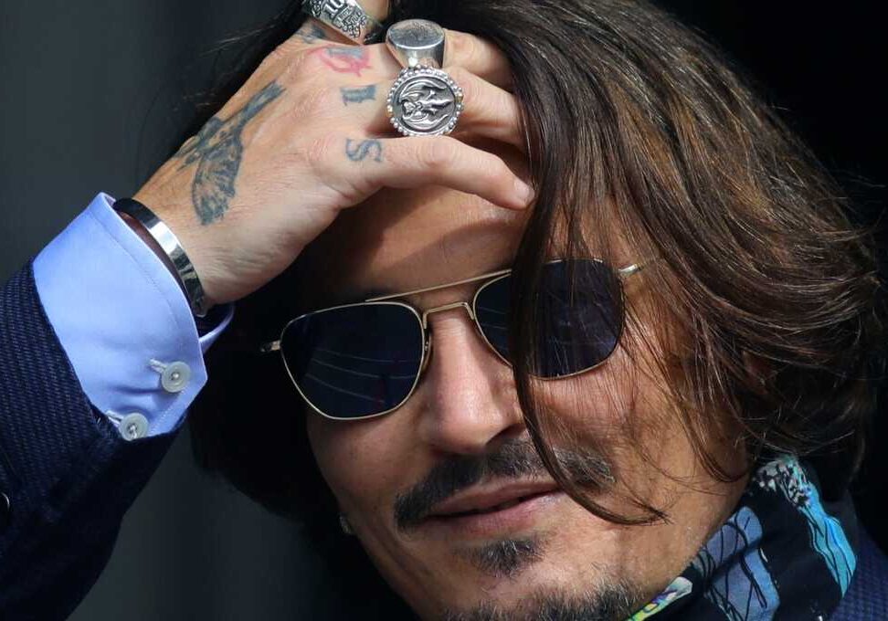 Man wearing sunglasses and rings, adjusting hair.